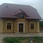Ukończony dom w Murowanej Goślinie — żółta elewacja, czerwona dachówka karpiówka, wole oko