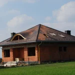 Układanie dachówki przy wolu oku — dom w budowie podczas realizacji dachu